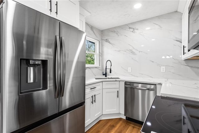 kitchen with a sink, light stone counters, tasteful backsplash, dark wood finished floors, and stainless steel appliances