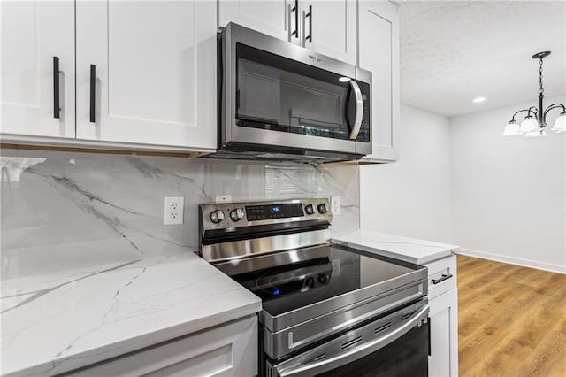 kitchen featuring light stone countertops, decorative backsplash, hanging light fixtures, white cabinets, and appliances with stainless steel finishes