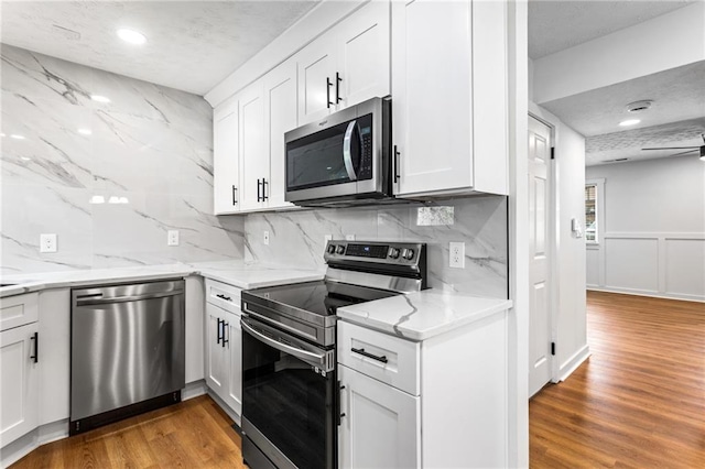 kitchen with light wood-style flooring, light stone counters, a textured ceiling, white cabinetry, and appliances with stainless steel finishes