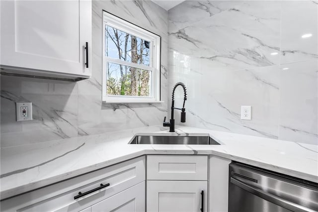 kitchen featuring a sink, light stone counters, stainless steel dishwasher, white cabinets, and decorative backsplash