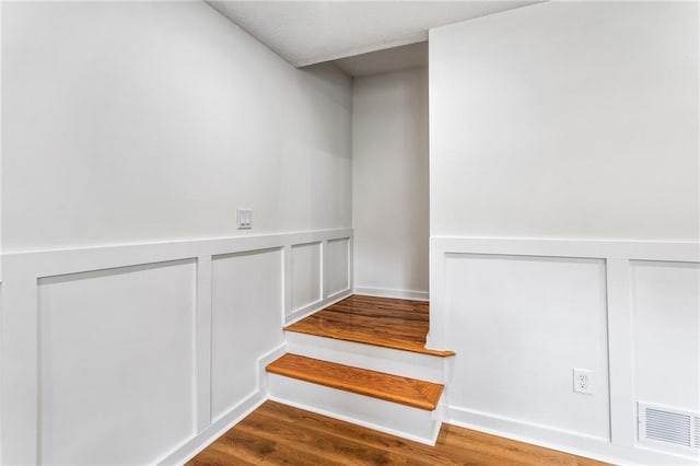 staircase featuring visible vents, a wainscoted wall, wood finished floors, and a decorative wall