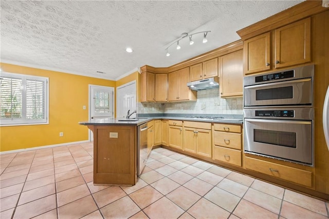 kitchen with appliances with stainless steel finishes, decorative backsplash, light tile patterned floors, sink, and kitchen peninsula