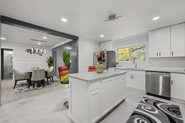 kitchen with appliances with stainless steel finishes, light stone counters, a kitchen island, sink, and white cabinetry