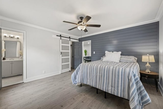 bedroom with crown molding, ensuite bath, ceiling fan, a barn door, and light hardwood / wood-style floors