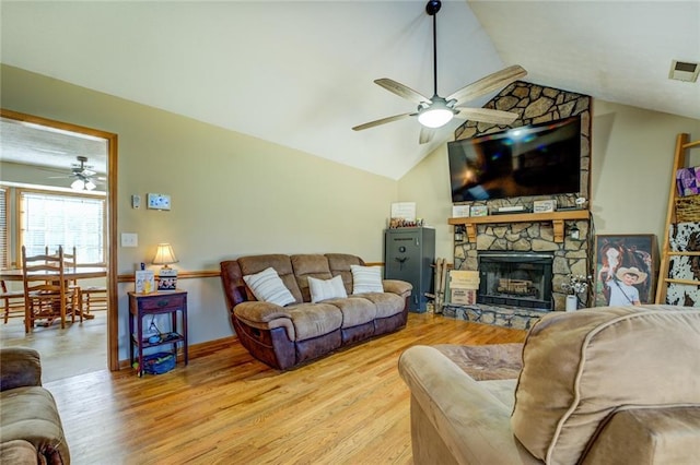 living area featuring a ceiling fan, lofted ceiling, a stone fireplace, and wood finished floors