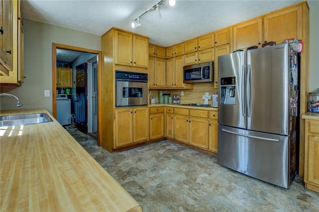 kitchen with stainless steel appliances, butcher block countertops, a sink, decorative backsplash, and washer / clothes dryer