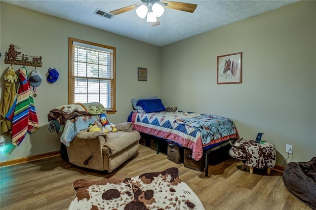 bedroom with ceiling fan, a textured ceiling, visible vents, and wood finished floors