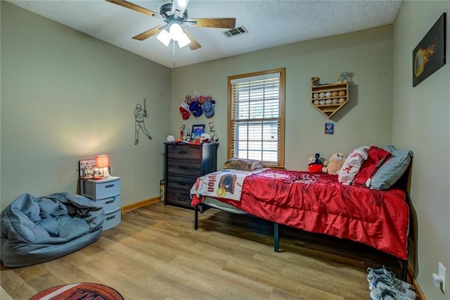 bedroom featuring visible vents, a ceiling fan, a textured ceiling, wood finished floors, and baseboards