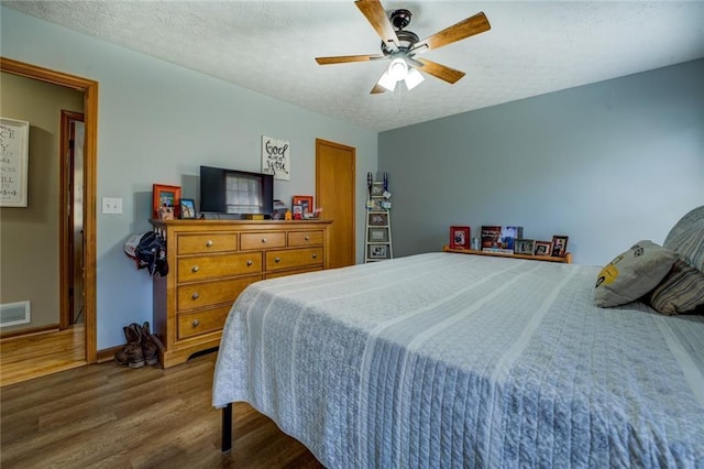 bedroom featuring visible vents, a textured ceiling, baseboards, and wood finished floors