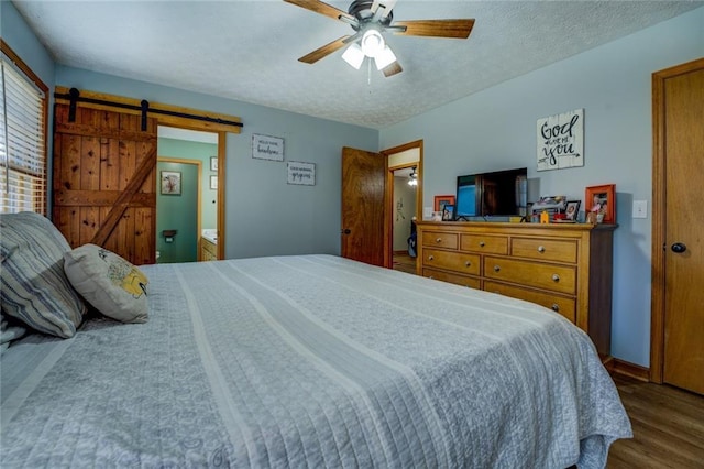 bedroom featuring a barn door, a ceiling fan, a textured ceiling, wood finished floors, and baseboards