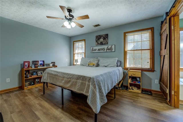 bedroom with a textured ceiling, a barn door, wood finished floors, and visible vents