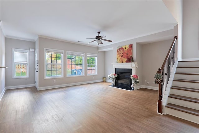 unfurnished living room featuring ceiling fan, a glass covered fireplace, stairs, wood finished floors, and ornamental molding