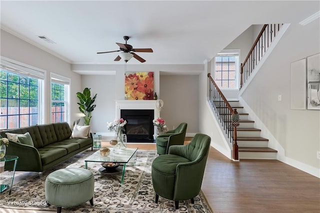 living area featuring a ceiling fan, visible vents, wood finished floors, stairway, and a glass covered fireplace