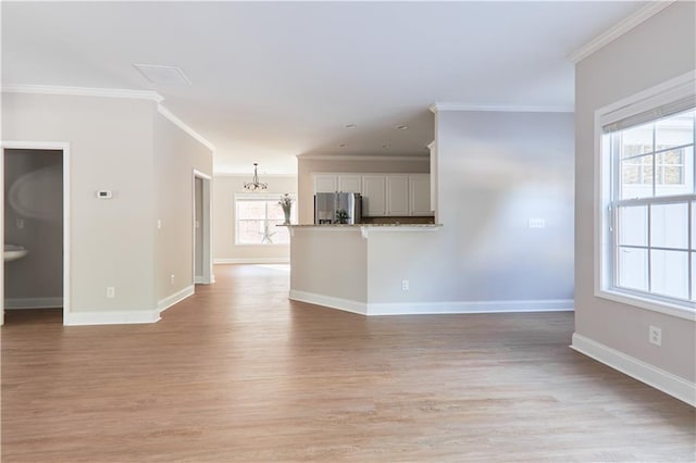 unfurnished living room featuring light wood-style floors, baseboards, ornamental molding, and a chandelier
