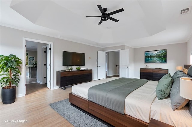 bedroom featuring light wood-style floors, baseboards, a tray ceiling, visible vents, and ornamental molding