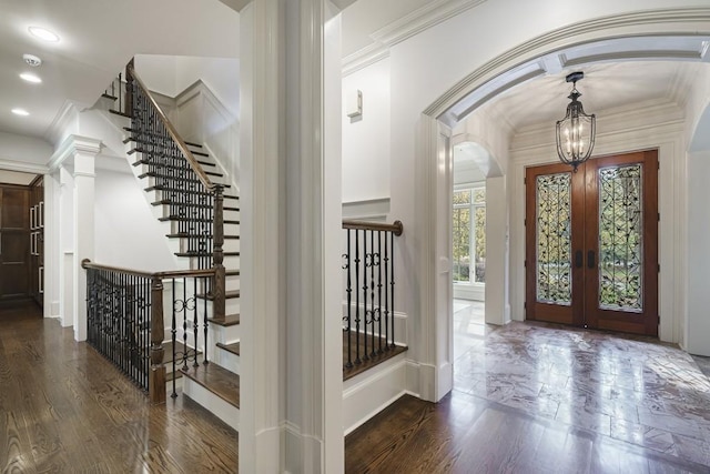 foyer entrance featuring dark wood-type flooring, decorative columns, a chandelier, ornamental molding, and french doors