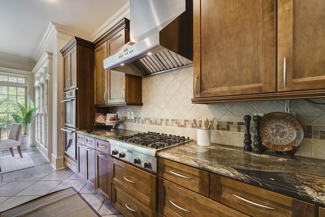 kitchen with dark stone counters, backsplash, stainless steel appliances, and wall chimney range hood