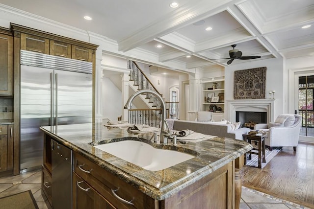 kitchen featuring ceiling fan, appliances with stainless steel finishes, sink, dark stone countertops, and a center island with sink