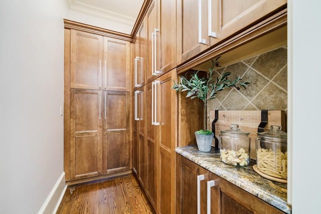 interior space featuring ornamental molding, light stone counters, tasteful backsplash, and dark hardwood / wood-style floors