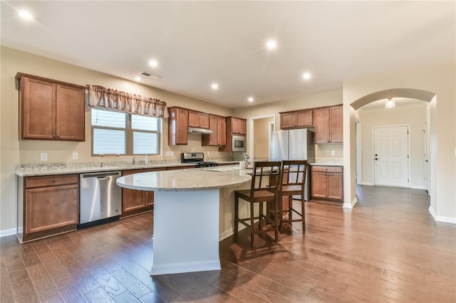 kitchen with a center island, light stone countertops, appliances with stainless steel finishes, dark hardwood / wood-style flooring, and a breakfast bar area