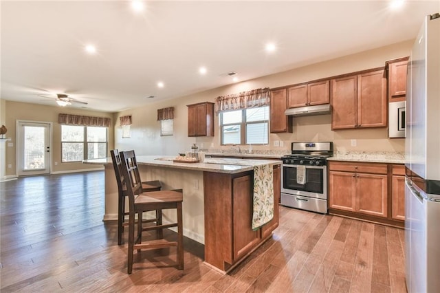 kitchen featuring hardwood / wood-style floors, a kitchen breakfast bar, a kitchen island, light stone countertops, and gas stove