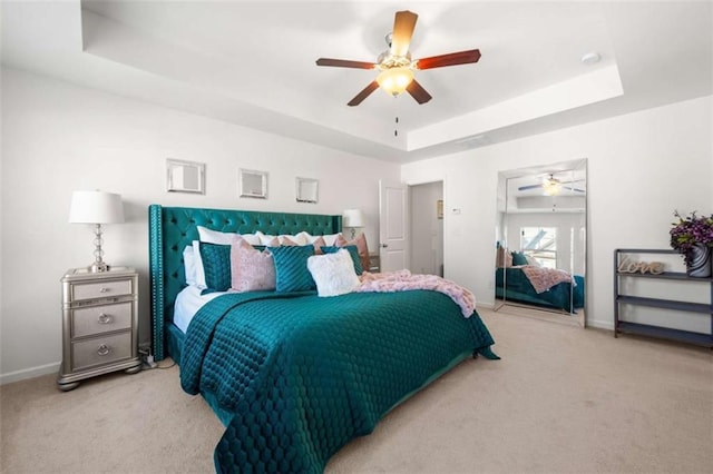 carpeted bedroom with a raised ceiling, baseboards, and a ceiling fan