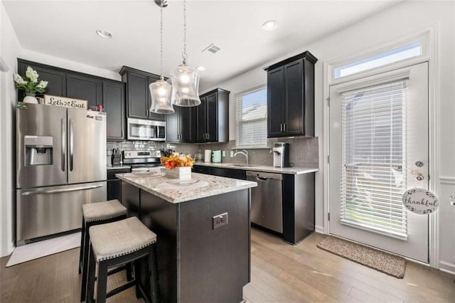 kitchen with visible vents, hanging light fixtures, stainless steel appliances, backsplash, and a kitchen island