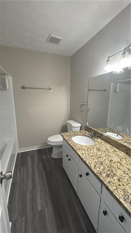 bathroom with visible vents, toilet, a textured ceiling, vanity, and wood finished floors