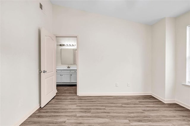 unfurnished bedroom with ensuite bath, sink, light hardwood / wood-style flooring, and lofted ceiling