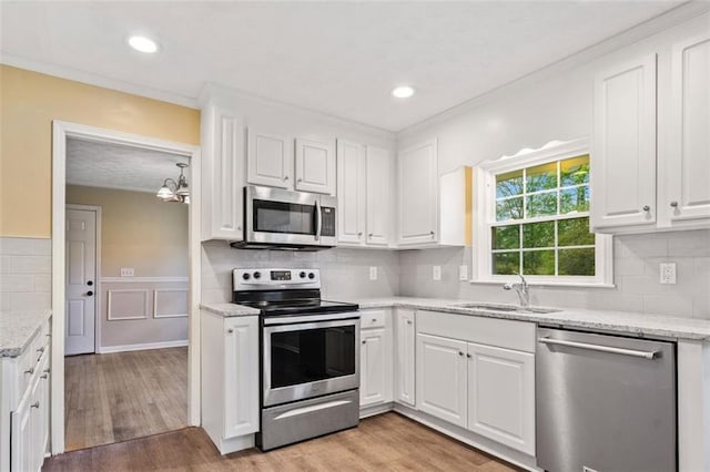 kitchen with stainless steel appliances, light wood-style flooring, a sink, tasteful backsplash, and white cabinetry