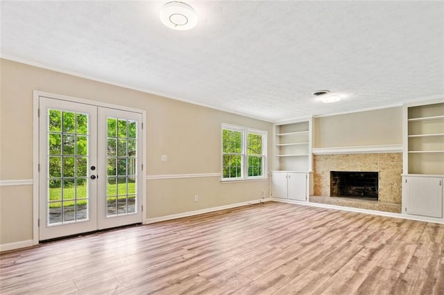 unfurnished living room with wood finished floors, a textured ceiling, a fireplace with raised hearth, french doors, and baseboards