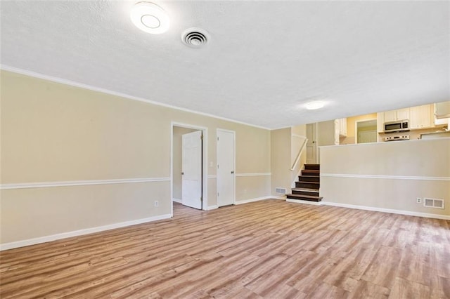unfurnished living room with baseboards, light wood-style flooring, visible vents, and stairway