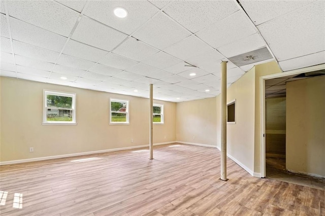 below grade area with plenty of natural light, baseboards, a drop ceiling, and light wood-style flooring
