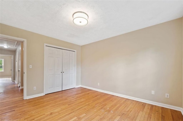 unfurnished bedroom with attic access, baseboards, light wood-style floors, and a textured ceiling