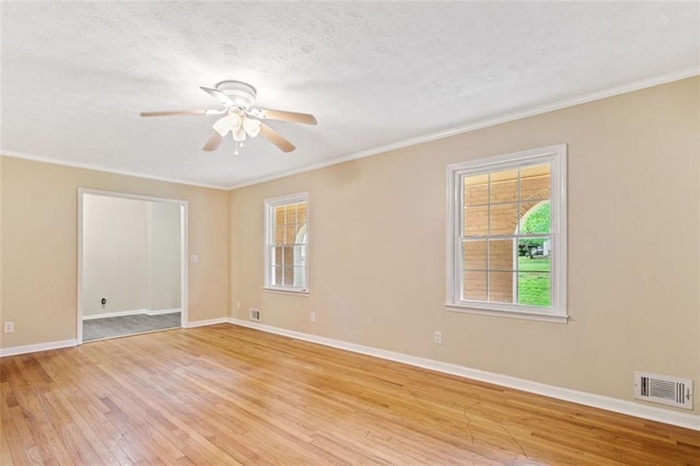 empty room featuring ornamental molding, light wood-style floors, visible vents, and plenty of natural light