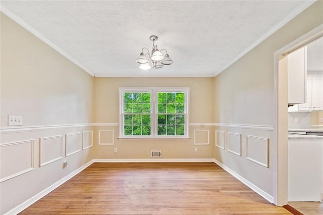 empty room featuring ornamental molding, a chandelier, visible vents, and light wood-style floors