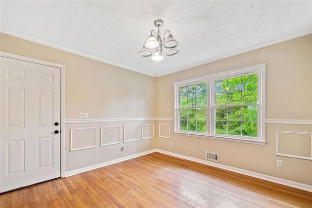 empty room featuring an inviting chandelier, visible vents, crown molding, light wood-style flooring, and a textured ceiling