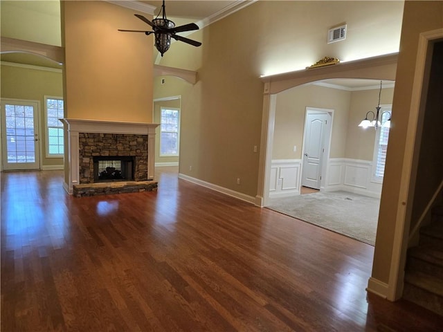 unfurnished living room with a stone fireplace, ceiling fan with notable chandelier, wood finished floors, visible vents, and ornamental molding