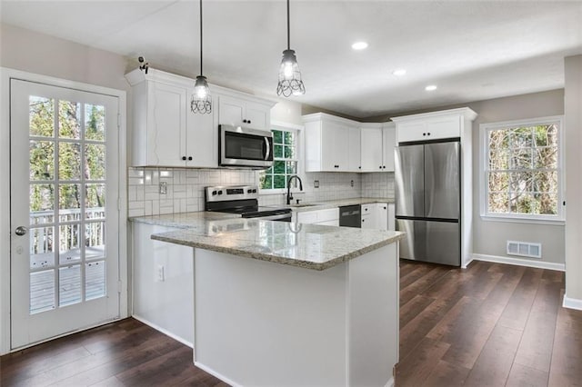 kitchen with light stone countertops, stainless steel appliances, sink, white cabinetry, and hanging light fixtures