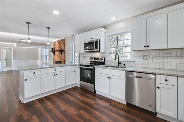 kitchen featuring kitchen peninsula, stainless steel appliances, sink, white cabinetry, and hanging light fixtures