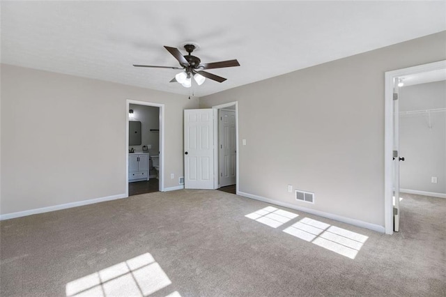 unfurnished bedroom with ensuite bath, a spacious closet, ceiling fan, light carpet, and a closet