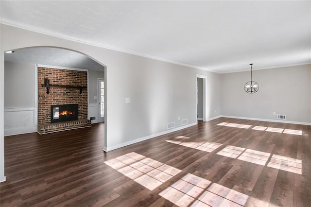 unfurnished living room featuring ornamental molding, dark wood-type flooring, a brick fireplace, and a notable chandelier