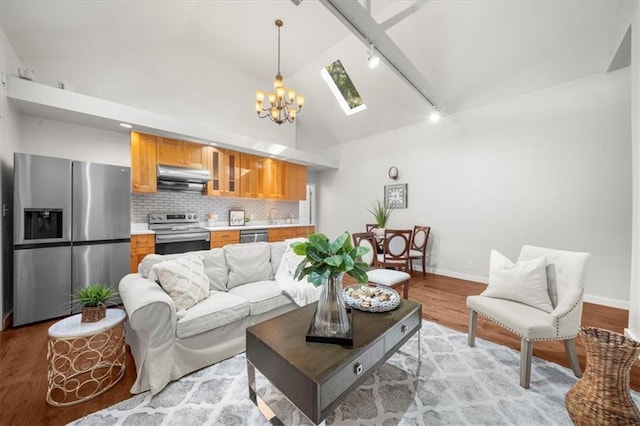 living room featuring light wood-type flooring, high vaulted ceiling, a skylight, track lighting, and a notable chandelier