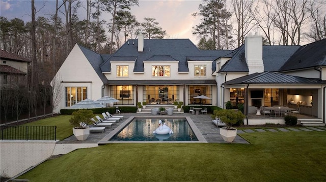 rear view of house featuring a yard, a patio, a chimney, and a standing seam roof