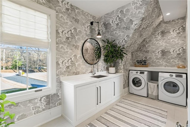 laundry room with wallpapered walls, light tile patterned floors, washer and dryer, cabinet space, and a sink