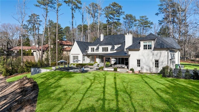 rear view of house featuring stucco siding, a lawn, fence, a chimney, and a patio area