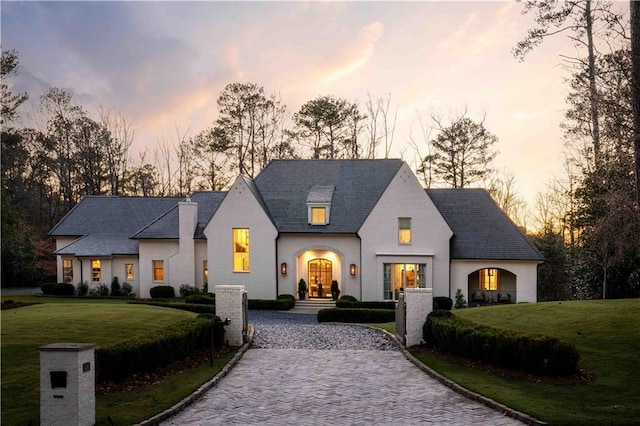 french country home featuring decorative driveway and a yard