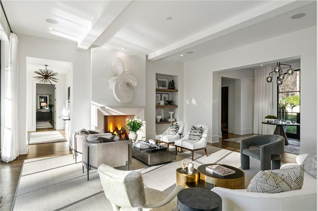 living room featuring wood finished floors, baseboards, beam ceiling, a warm lit fireplace, and a notable chandelier