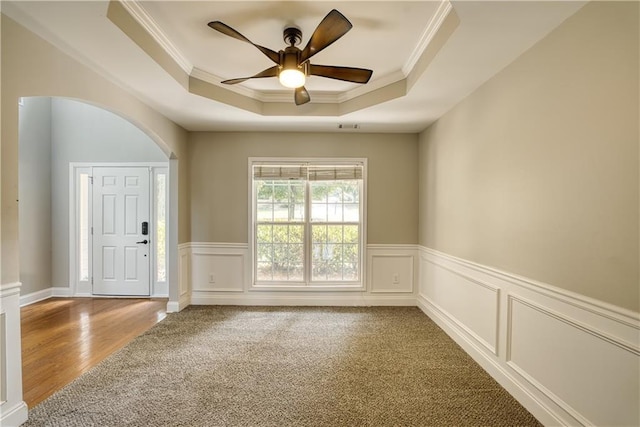 carpeted spare room with a raised ceiling, crown molding, and ceiling fan