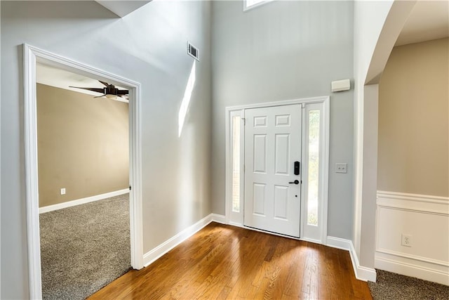 entryway with ceiling fan, wood-type flooring, and a towering ceiling